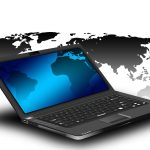 An open laptop with a blue screen placed in front of a world map.