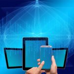 A hand holding a smartphone in front of three tablets doing keyword research.